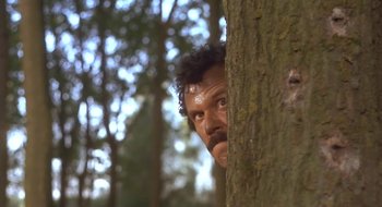 Movie still from “Black Cat, White Cat” (1998), directed by Emir Kusturica – A person peering around a tree; Medium shot, Low angle