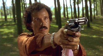 Movie still from “Black Cat, White Cat” (1998), directed by Emir Kusturica – A man holding a gun in a forest; Close Up shot, Low angle