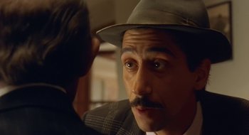 Movie still from “Black Cat, White Cat” (1998), directed by Emir Kusturica – A person wearing a hat and a suit; Close Up shot, Over the shoulder angle