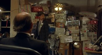 Movie still from “Black Cat, White Cat” (1998), directed by Emir Kusturica – A man standing in a room filled with lots of boxes; Medium shot, Over the shoulder angle