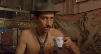 Movie still from “Black Cat, White Cat” (1998), directed by Emir Kusturica – A man with a mustache and hat drinking a cup of coffee; Close Up shot, Low angle