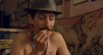 Movie still from “Black Cat, White Cat” (1998), directed by Emir Kusturica – A man with a mustache wearing a hat and sitting on a couch; Close Up shot, Low angle