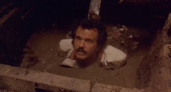 Movie still from “Black Cat, White Cat” (1998), directed by Emir Kusturica – A man with a beard is laying on the ground in the mud; Close Up shot, High angle