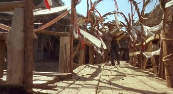 Movie still from “Black Cat, White Cat” (1998), directed by Emir Kusturica – A man carrying a box walking down a street; Wide shot, Low angle