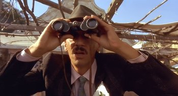 Movie still from “Black Cat, White Cat” (1998), directed by Emir Kusturica – A man in a suit looking through binoculars; Close Up shot, Low angle