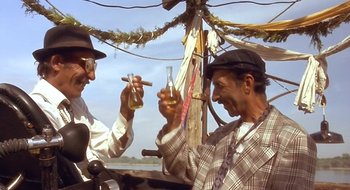 Movie still from “Black Cat, White Cat” (1998), directed by Emir Kusturica – A couple of people that are drinking some alcohol; Medium shot, Low angle