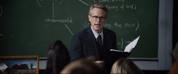 Movie still from “Black Christmas” (2019), directed by Sophia Takal – A man in a suit and tie is holding a book; Medium shot, Over the shoulder angle