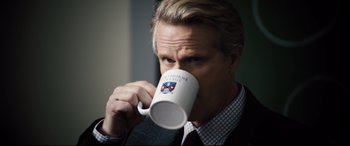 Movie still from “Black Christmas” (2019), directed by Sophia Takal – A man in a suit drinking from a coffee mug; Close Up shot, Over the shoulder angle