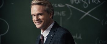 Movie still from “Black Christmas” (2019), directed by Sophia Takal – A man wearing a suit and tie standing in front of a chalkboard; Close Up shot, Over the shoulder angle