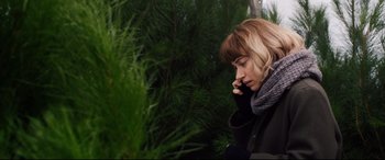 Movie still from “Black Christmas” (2019), directed by Sophia Takal – A woman is talking on a cell phone in front of some trees; Close Up shot, High angle