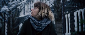 Movie still from “Black Christmas” (2019), directed by Sophia Takal – A woman wearing a black coat and a blue scarf; Close Up shot, Low angle