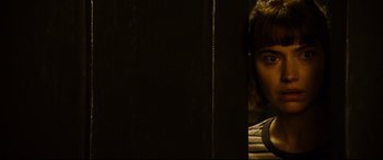 Movie still from “Black Christmas” (2019), directed by Sophia Takal – A woman peeking out from behind a wooden wall; Close Up shot, Over the shoulder angle