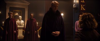 Movie still from “Black Christmas” (2019), directed by Sophia Takal – A man in a purple robe standing next to another man in a red robe; Medium shot, Over the shoulder angle