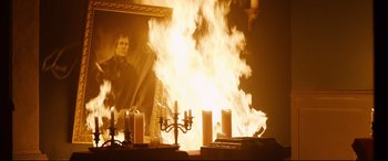 Movie still from “Black Christmas” (2019), directed by Sophia Takal – A fire is burning in the middle of a room with candles; Medium shot, Over the shoulder angle
