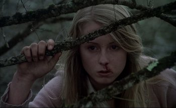 Movie still from “Black Moon” (1975), directed by Louis Malle – A woman with a knife in her mouth behind a tree branch; Close Up shot, Low angle