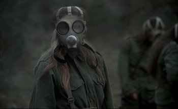 Movie still from “Black Moon” (1975), directed by Louis Malle – A woman wearing a gas mask in the woods; Medium shot, Over the shoulder angle