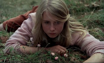 Movie still from “Black Moon” (1975), directed by Louis Malle – A girl laying in the grass looking at the camera; Close Up shot, High angle