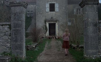 Movie still from “Black Moon” (1975), directed by Louis Malle – A woman is walking down a path in front of an old building; Wide shot, High angle