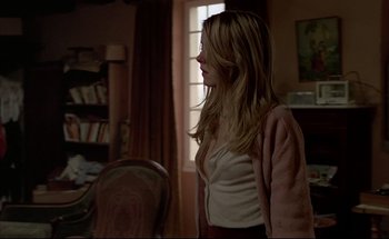 Movie still from “Black Moon” (1975), directed by Louis Malle – A woman standing in a living room with a book case in the background; Medium shot, Over the shoulder angle