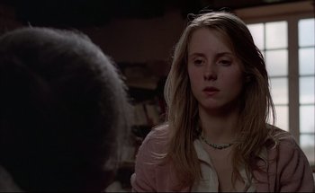 Movie still from “Black Moon” (1975), directed by Louis Malle – A woman with blonde hair and a green necklace looking into the camera; Close Up shot, Over the shoulder angle