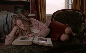 Movie still from “Black Moon” (1975), directed by Louis Malle – A girl is laying on the couch reading a book; Medium shot, High angle