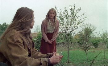 Movie still from “Black Moon” (1975), directed by Louis Malle – Two women are standing in the grass near a tree; Medium shot, Over the shoulder angle
