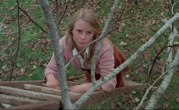 Movie still from “Black Moon” (1975), directed by Louis Malle – A young girl sitting on a wooden platform; Medium shot, High angle