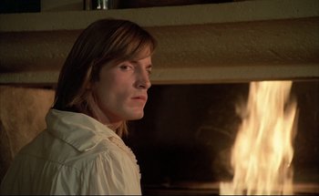 A woman in a white shirt is standing in front of a fireplace