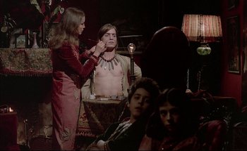 Movie still from “Black Moon” (1975), directed by Louis Malle – A woman is painting a man's chest with a brush; Medium shot, Over the shoulder angle
