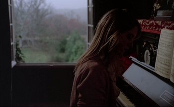 Movie still from “Black Moon” (1975), directed by Louis Malle – A woman standing in front of an open window playing a piano; Medium shot, Over the shoulder angle
