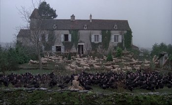 Movie still from “Black Moon” (1975), directed by Louis Malle – A flock of sheep are gathered in front of a house; Extreme Wide shot, High angle