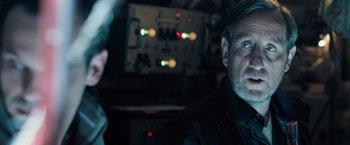 Movie still from “Black Sea” (2014), directed by Kevin Macdonald – A man in a black shirt is looking at the camera; Close Up shot, Over the shoulder angle