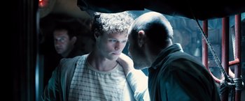 Movie still from “Black Sea” (2014), directed by Kevin Macdonald – A man standing next to another man in the dark; Close Up shot, Over the shoulder angle