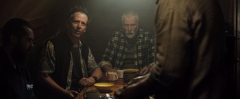 Movie still from “Black Sea” (2014), directed by Kevin Macdonald – A group of men sitting at a wooden table with cups; Medium shot, Over the shoulder angle
