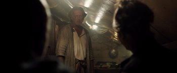 Movie still from “Black Sea” (2014), directed by Kevin Macdonald – An old man in an old - fashioned outfit standing in a kitchen; Medium shot, Over the shoulder angle