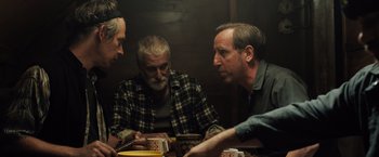 Movie still from “Black Sea” (2014), directed by Kevin Macdonald – A group of people sitting around a table; Medium shot, Over the shoulder angle