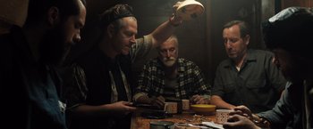 Movie still from “Black Sea” (2014), directed by Kevin Macdonald – Two men sitting at a wooden table and one of the men is using a cell phone; Medium shot, Low angle