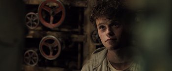 Movie still from “Black Sea” (2014), directed by Kevin Macdonald – A young man with curly brown hair is looking at the camera; Close Up shot, Over the shoulder angle