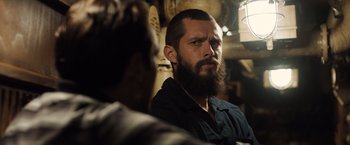 Movie still from “Black Sea” (2014), directed by Kevin Macdonald – A man with a beard is looking at the camera; Close Up shot, Over the shoulder angle