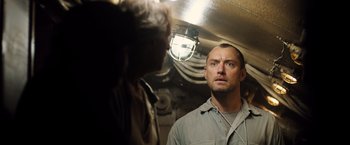 Movie still from “Black Sea” (2014), directed by Kevin Macdonald – A man standing next to another man in a room; Close Up shot, Low angle