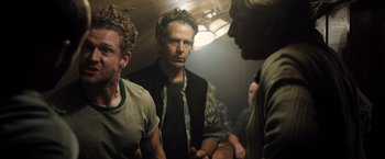 Movie still from “Black Sea” (2014), directed by Kevin Macdonald – A group of men standing around in a room together; Medium shot, Over the shoulder angle