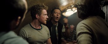 Movie still from “Black Sea” (2014), directed by Kevin Macdonald – Two men are standing in front of another man in a room; Medium shot, Over the shoulder angle