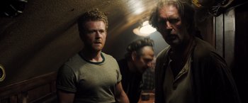 Movie still from “Black Sea” (2014), directed by Kevin Macdonald – A group of men standing next to each other in a room; Medium shot, Over the shoulder angle