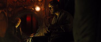Movie still from “Black Sea” (2014), directed by Kevin Macdonald – A man sitting in a dimly - lit room holding a cell phone; Medium shot, Low angle