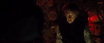 Movie still from “Black Sea” (2014), directed by Kevin Macdonald – A man standing in front of a bunch of wall hangings; Close Up shot, Over the shoulder angle