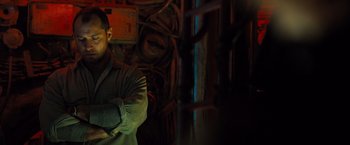 Movie still from “Black Sea” (2014), directed by Kevin Macdonald – A man standing with his arms crossed in front of a wall; Medium shot, Low angle