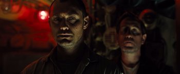 Movie still from “Black Sea” (2014), directed by Kevin Macdonald – A man standing next to another man in a dark room; Close Up shot, Low angle