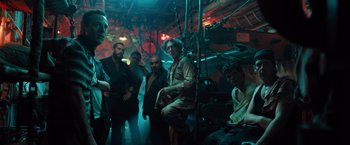 Movie still from “Black Sea” (2014), directed by Kevin Macdonald – A group of people standing around in a room; Medium shot, Low angle
