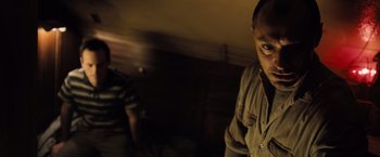 Movie still from “Black Sea” (2014), directed by Kevin Macdonald – A man standing next to another man in a dark room; Close Up shot, Low angle
