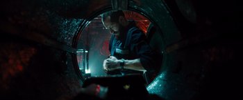 Movie still from “Black Sea” (2014), directed by Kevin Macdonald – A man working in an industrial setting in a dark room; Medium shot, Low angle